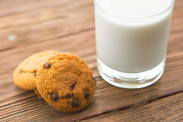 Chocolate chip cookies and a glass of milk on wooden table