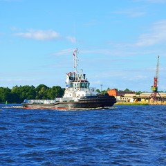 A tug boat sailing against port cranes in a port in Latvia