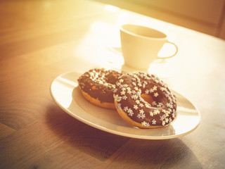 Chocolate donuts sprinkled with colorful stars on the table. Coffee decorations in the background. Donut on table. Chocolate donut at sunrise. Coffee and donut.