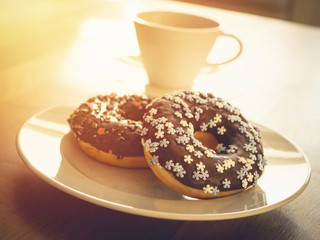 Chocolate donuts sprinkled with colorful stars on the table. Coffee decorations in the background. Donut on table. Chocolate donut at sunrise. Coffee and donut.