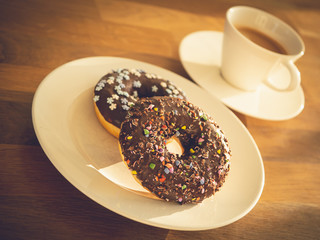 Chocolate donuts sprinkled with colorful stars on the table. Coffee decorations in the background. Donut on table. Chocolate donut at sunrise. Coffee and donut.