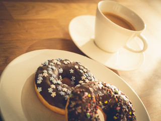 Chocolate donuts sprinkled with colorful stars on the table. Coffee decorations in the background. Donut on table. Chocolate donut at sunrise. Coffee and donut.