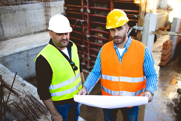 Men in hardhat and yellow and orange jacket posing on building site