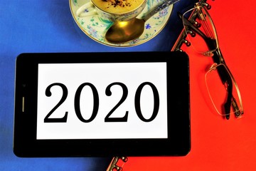 2020-message on tablet computer. New year, office folder, coffee in a Cup for cheerfulness, reading glasses.