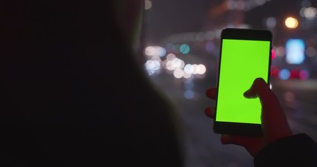 Faceless woman holding mobile phone with mock up screen on defocused night street background. Female hands typing scrolling smartphone outdoors in evening city slow motion. App store technologies