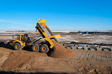Rock Truck dumping load of sandy granular material on galvanized metal mechanically stabilized earth strips attached to the back of concrete MSE wall panels on the Regina Bypass freeway project. 