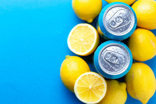 Soda cans with condensation drops and lemons over blue background