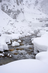 White snowing covered the mountain and stones on freezing river with snow monkeys sitting under snow storm background over sky winter season, Japan