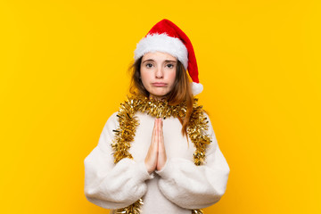Girl with christmas hat over isolated yellow background pleading