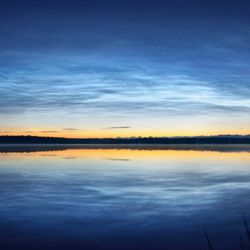 Bright noctilucent clouds over a lake in Latvia on a summer night