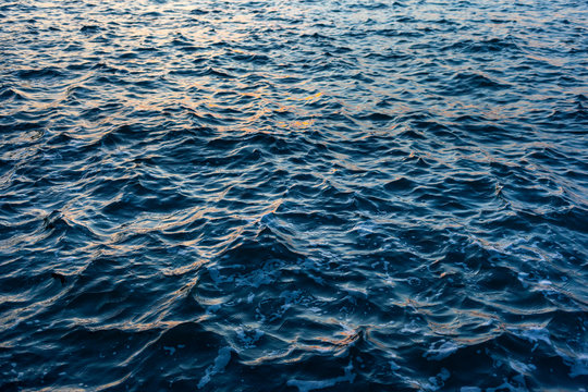 Dark blue Sea water with a choppy  texture and reflected orange highlights from a sunset