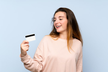 Fototapeta premium Young brunette girl over isolated blue background holding a credit card