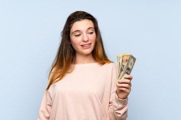 Young brunette girl over isolated blue background taking a lot of money