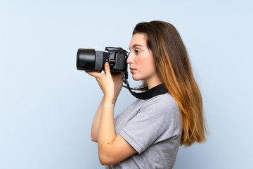 Young brunette girl over isolated blue background with a professional camera
