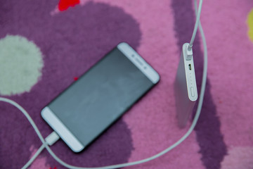 Smartphone Charging with silver Power Bank Through Spiral USB Cable . Smartphone charging with power bank on pink carpet . Phone charging with energy bank .