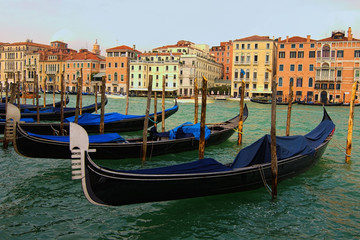 Venice, Italy-September 28, 2019: Classic landscape of Venice. Old black gondolas moored near wooden mooring poles. Scenic Grand Canal with turquoise water with ancient colorful buildings
