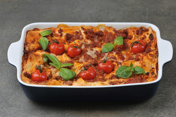 Lasagna with cherry tomatoes and fresh basil leaves.  Close-up.  Dark background.