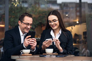 Business people in cafe, working while break. Business-team working on laptop at coffee bar, looking a mobile phone.