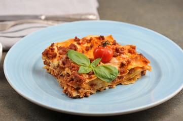 Serving of lasagna on a light plate.  Lasagna garnished with cherry tomatoes and fresh basil leaves.  Close-up.