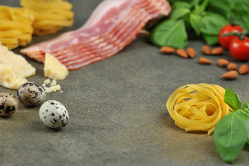 Set for cooking pasta carbonara.  Pasta, basil, bacon, cheese and quail eggs on a dark surface.  Free space for text.