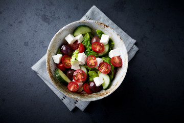 Fototapeta na wymiar Salad with Kalamata Olives, Cucumber Cherry Tomatoes and Feta Cheese on black Stone Background. Healthy Snack Idea. Top view. Copy space. 