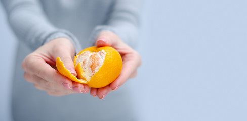 Woman holding and cleans tangerine on gray light background, space for text