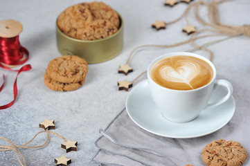 A cup of coffee and oatmeal cookies with pieces of chocolate. Red ribbon and decor create a festive mood concept. Light background.