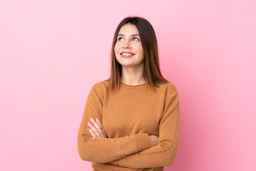 Young woman over isolated pink background looking up while smiling