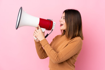 Young woman over isolated pink background shouting through a megaphone