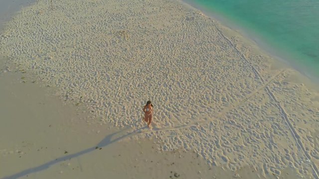 Cinematic aerial view of a woman alone on isolated white sandbar in Onok island in Balabac, Philippines. Girl sunbathing at the paradise tropical island in Philippines