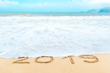 Inscription, letters 2019 on the wet sand on the background of the sea wave washing away with water. Text on the beach. New year concept. End of 2019.