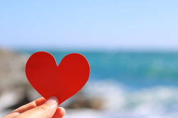 Red heart card in a hand on a background of the sea