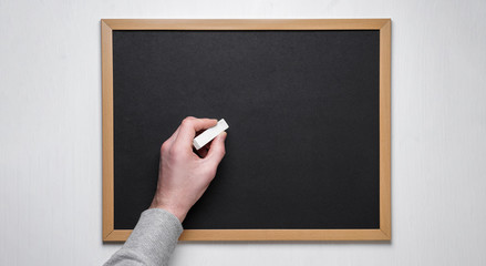 Male hand with chalk on the empty blackboard or chalkboard.