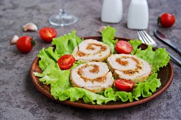 Cold appetizer, sliced baked pork roll with fried carrots and onions on fresh lettuce leaves on a clay plate on a gray concrete background. Holiday recipes meat dishes.
