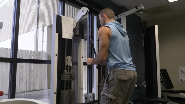 Man working out in the gym exercising, doing triceps pulldowns on a triceps pull down exercise machine.