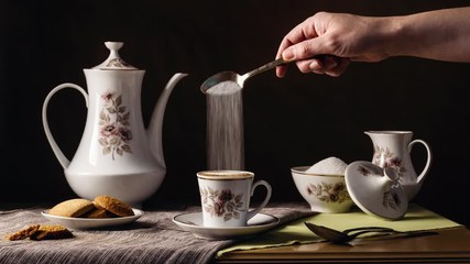 Cinemagraph of a person's hand continuously pouring sugar into a vintage cup of coffee on a table with cookies and the rest of the retro tableware. Dark background. Lifestyle - Powered by Adobe