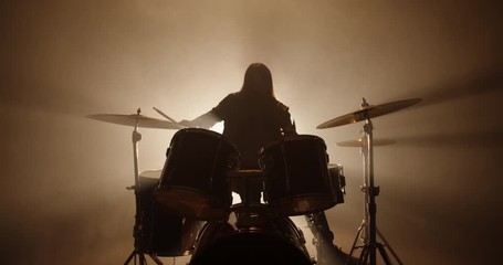 An authentic drummer playing a solo in a band, hitting the drums while playing rock or metal music, silhouetted on smoked stage - band, music concept 4k footage - Powered by Adobe