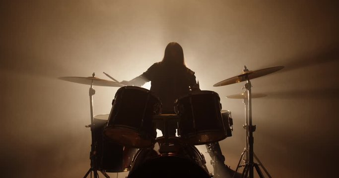 An authentic drummer playing a solo in a band, hitting the drums while playing rock or metal music, silhouetted on smoked stage - band, music concept 4k footage