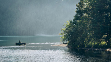 Fototapeta premium A boat with a fisherman sailing in the backlight against the background of the forest. Fishing in Siberia and Altai. Katunsky nature reserve.