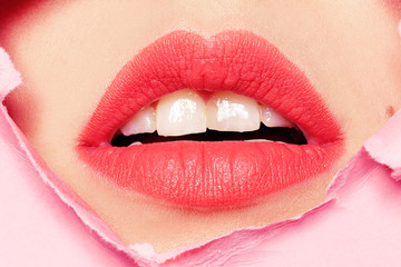Fototapeta premium Big beautiful lips, beauty salon, lip enhancement, Botox. Beautiful teeth, dentistry. Pink background, girl's face through torn cardboard.