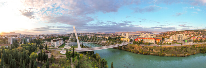 Podgorica, Montenegro: aerial view of Millennium bridge and Moraca river in the morning, at sunrise, under beautiful sky. Cable stayed bridge with green area in the foreground. 180 degree panorama.