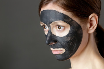 Charcoal face mask or black clay mud. Beautiful woman with black mask on her face, close up studio head shot. Natural cosmetic concept.