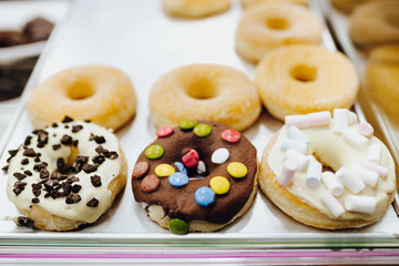 Doughnuts on the counter. Several flavors. Chocolate, cookies, marshmallow, white chocolate, icing sugar, frost, glazing. Calories counting and food control concept.