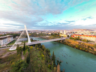 Podgorica, Montenegro: aerial view of the city featuring Millennium bridge and Moraca river in the morning, at sunrise, under beautiful sky. Cable stayed bridge with green area in the foreground.