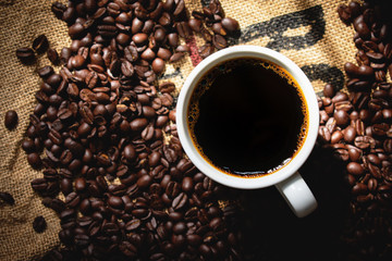 top view black coffee in white ceramic coffee cup with roasted coffee on background.morning light.