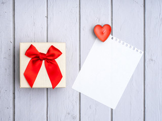 Flat lay yellow box with red bow and and  heart shaped candles and white sheet of paper on White wooden table Wedding card ideas and Valentines Day copy space for text