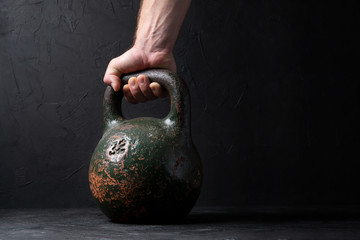 Man holds old heavy sports weight 32 kg on dark background