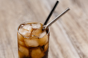 Close-up of a glass with soda and ice on a wooden table background. Black Silver Metal straw. 