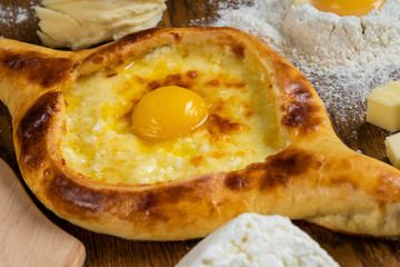 Adjarian Khachapuri with Adyghe cheese and egg yolks and slices of butter is on a wooden board sprinkled with flour.