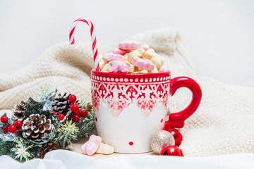 Red mug with marshmallows and winter ornaments on a white sheets